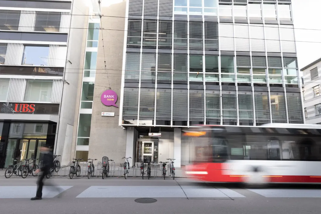 Vista exterior da filial BANK-now Winterthur com entrada e eléctrico a passar.