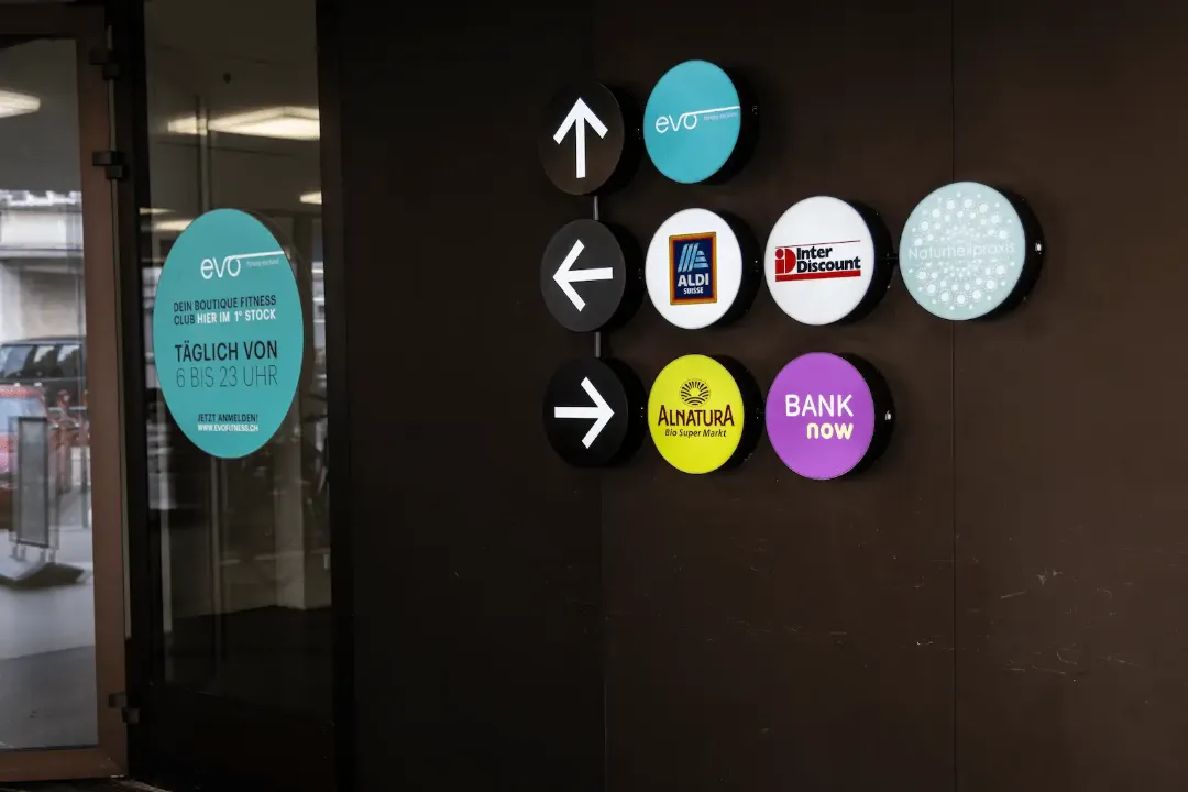 Sinalização na entrada da filial BANK-now Zurique-Oerlikon com logótipos e setas de direção.